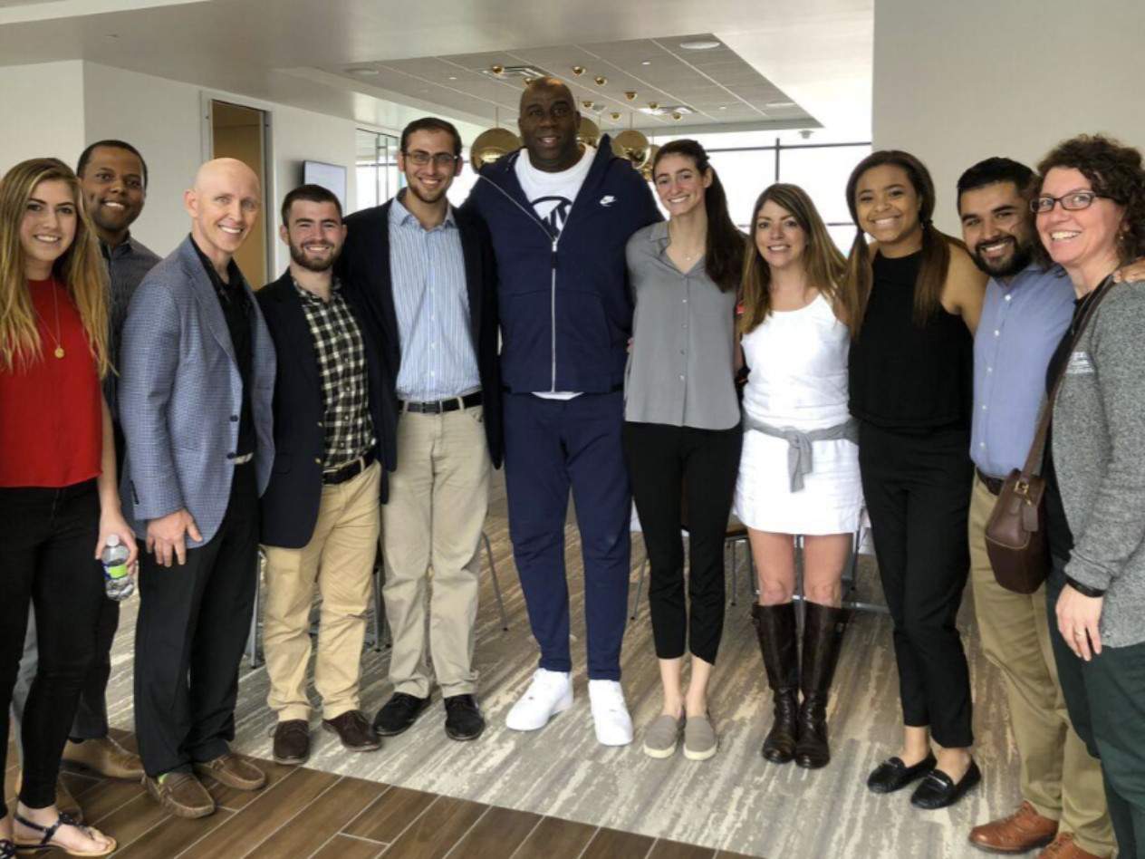 Earvin “Magic” Johnson, Los Angeles Lakers point guard for 13 seasons, stands with WashU students and staff at the Lakers practice facility in El Segundo, CA, on Monday, March 12, 2018. Said Rishe: “This was totally unexpected, and Magic couldn’t have been any nicer or more gracious.” Visitors with Magic include Michael Weisman, Taylor Cohen, Bryant Powell, Rishe, Issac Kaufer, Allan Bekerman, Magic Johnson, Kelly Minster, Teresa Iadevito, Katie Sissler, Oscar Vasco, and Konnie Henning.