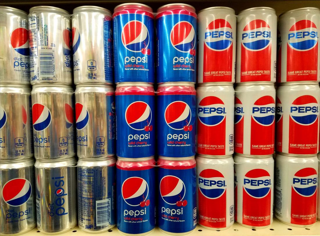 Cans of Pepsi sit on a grocery shelf.