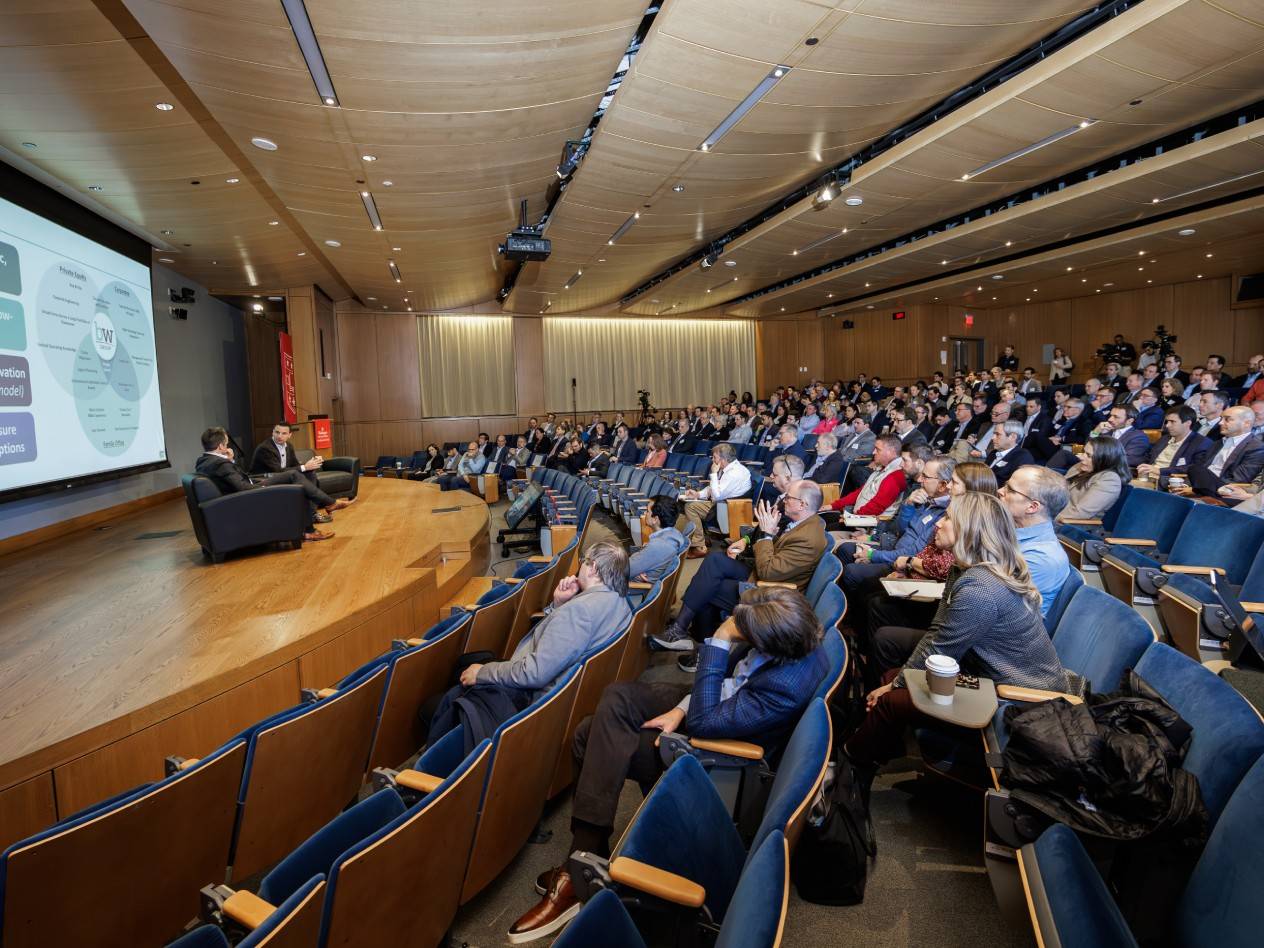 Side view of the Emerson Auditorium stage for the Familiy Business Symposium showing Peter Boumgarden and Kyle Chapman on stage with a packed house.