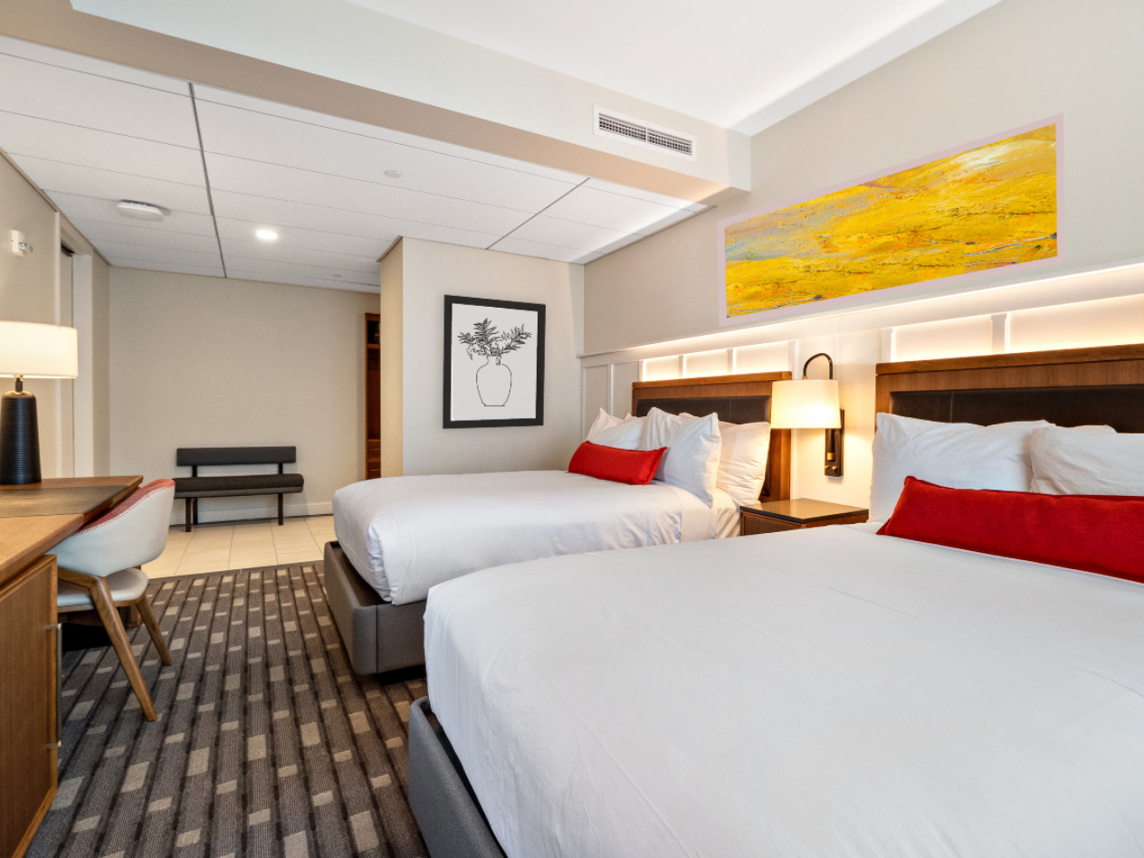 A hotel room with two beds and a desk, and artwork on the walls