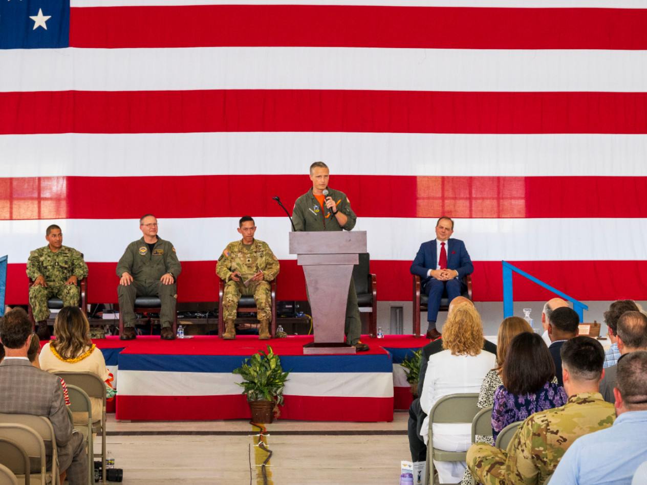 Man speaking in front of a large US flag