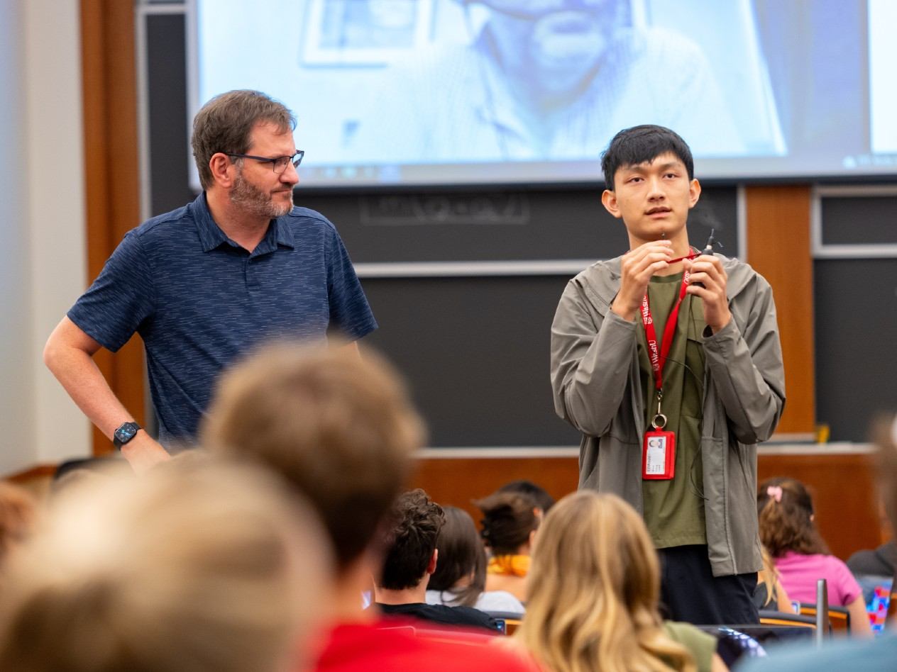 A teacher and student stand in front of a class