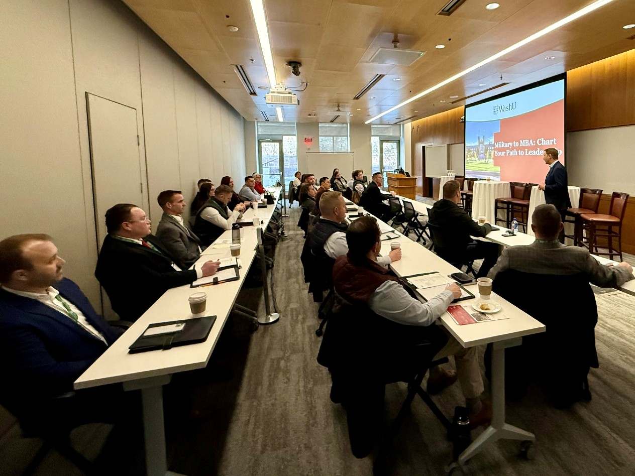 A man, standing, talks to a group of people at tables. A projected slide behind him reads: Military to MBA: Chart Your Path to Leadership