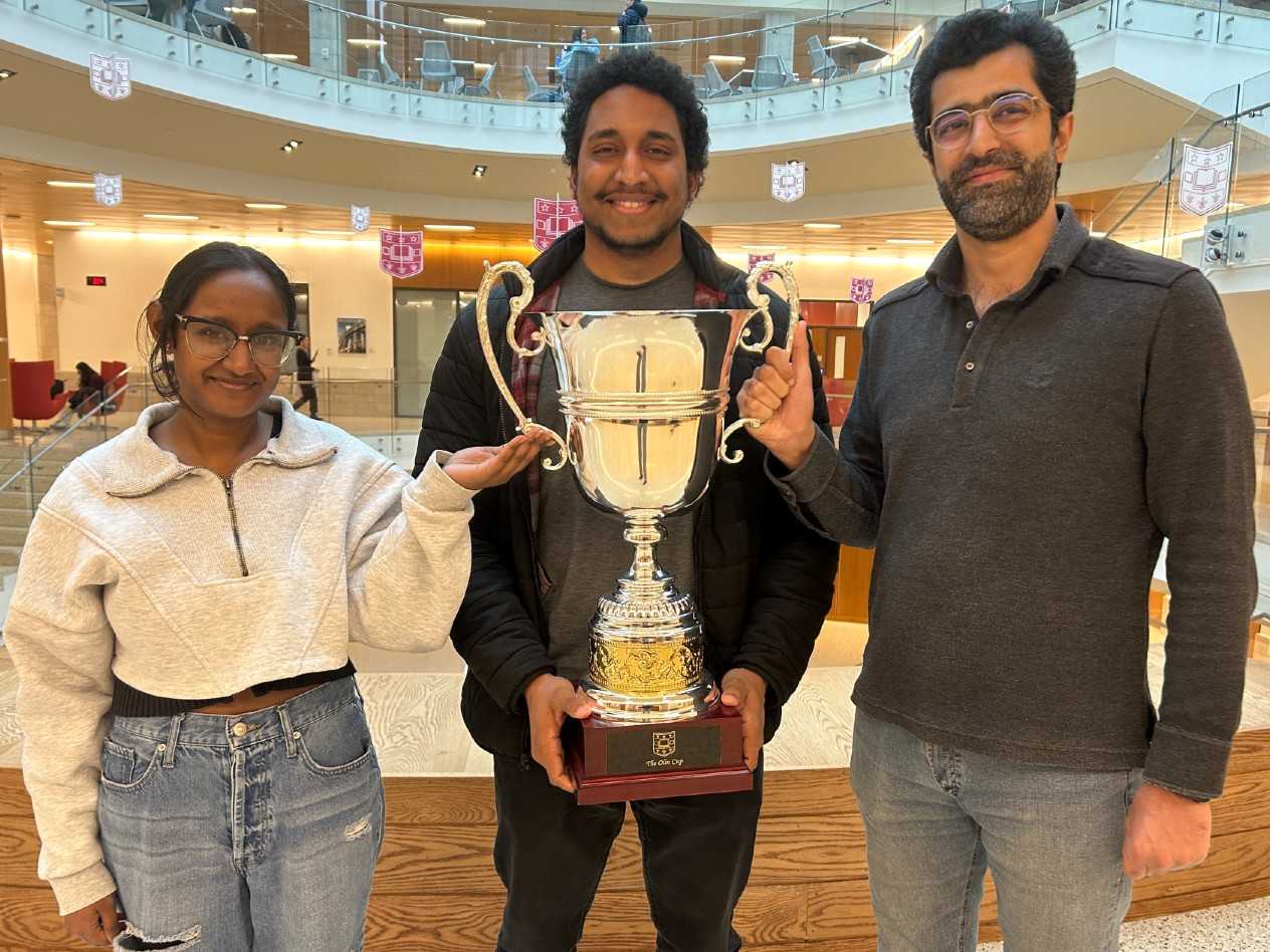 A woman and two men stand together holding a large trophy