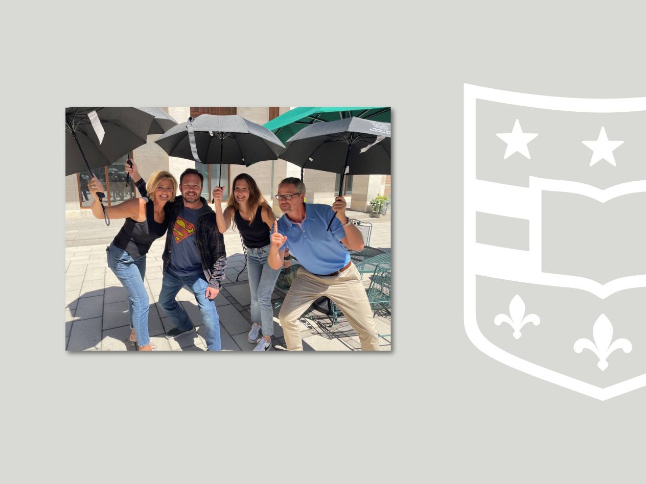 Four people smile at the camera, holding umbrellas on a sunny patio.