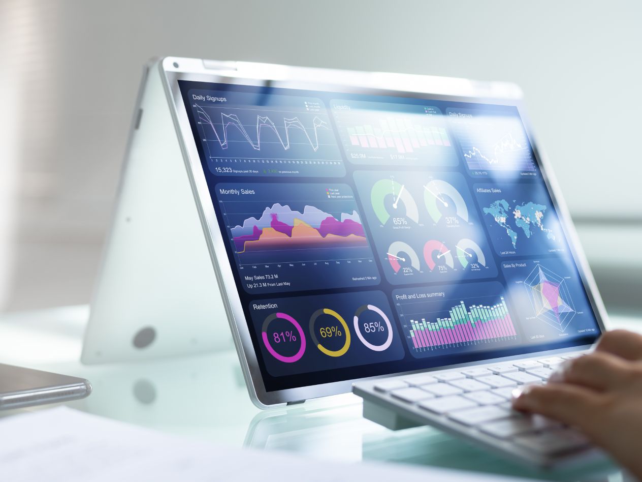Stylized closeup image of a computer screen with hands on the keyboard and a variety of graphs and charts on the screen.