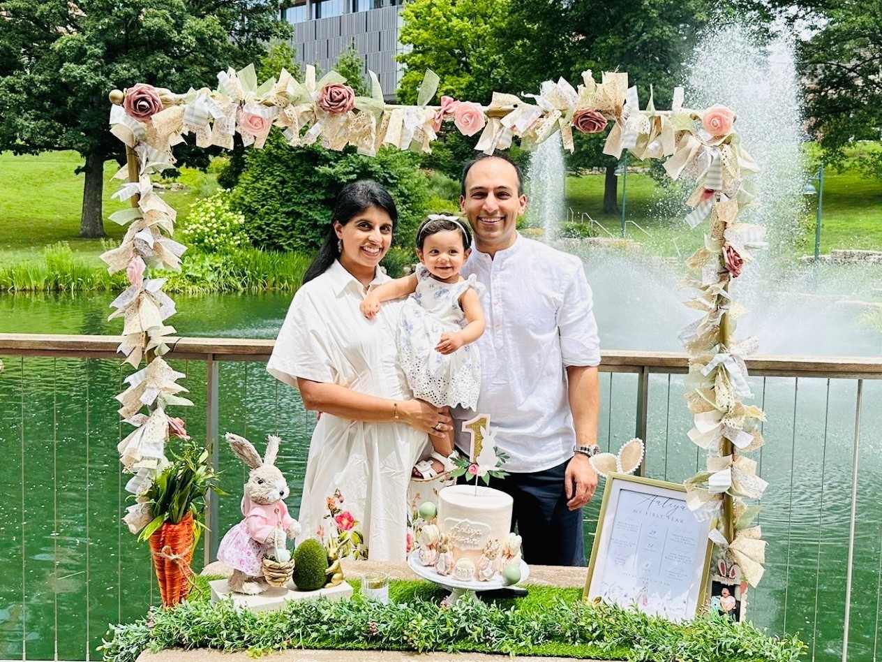 Parents hold a baby in a park setting with decorations