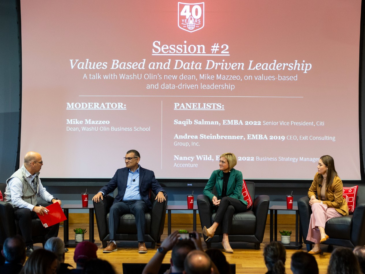 A group of people seated on a dais holding a discussion in front of an audience.